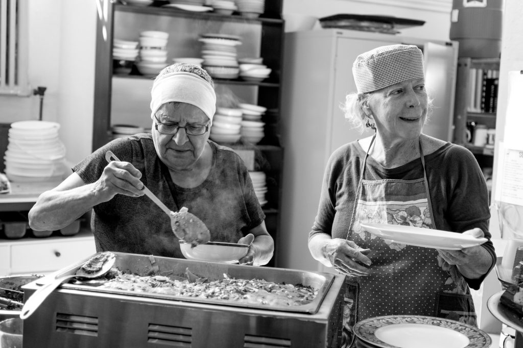 Volunteers serve a community meal from simple chafing dishes in the kitchen.